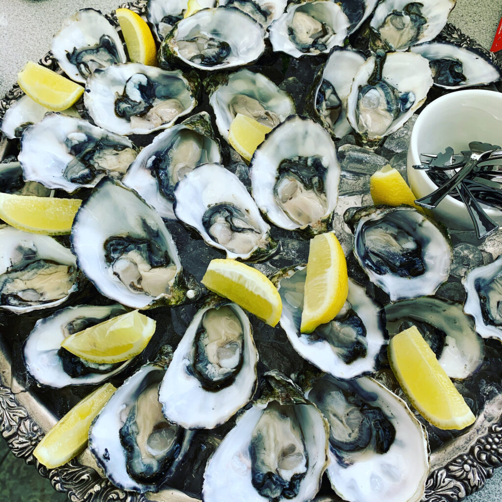 A platter of raw oysters with lemon wedges.
